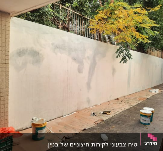 קיר צבוע חלקית עם דליי צבע וכלי עבודה